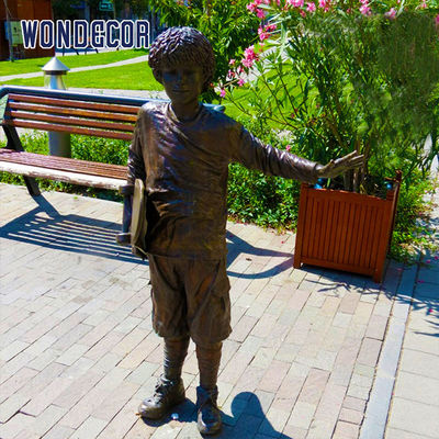 A bronze metal art sculpture of a boy holding a skateboard outdoors